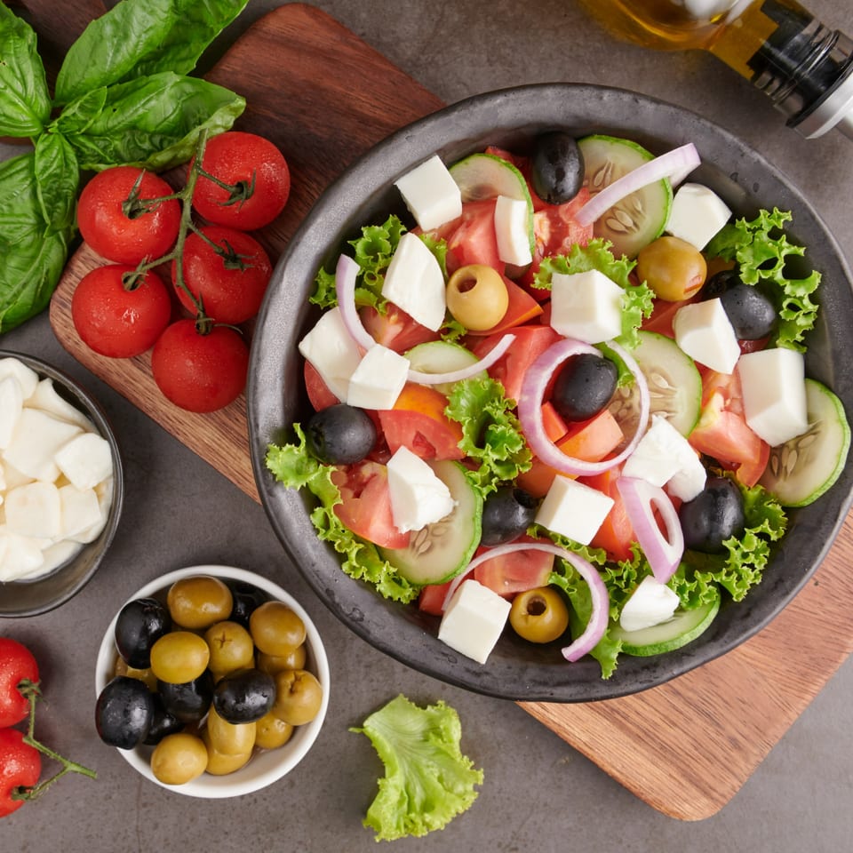 Fresh Greek salad with tomatoes, cucumbers, olives, feta, and red onion, served with basil and olive oil.