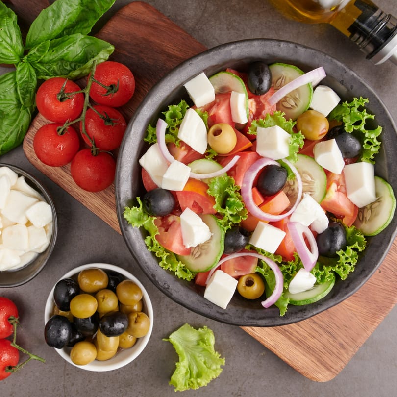 Fresh Greek salad with tomatoes, cucumbers, olives, feta, and red onion, served with basil and olive oil.