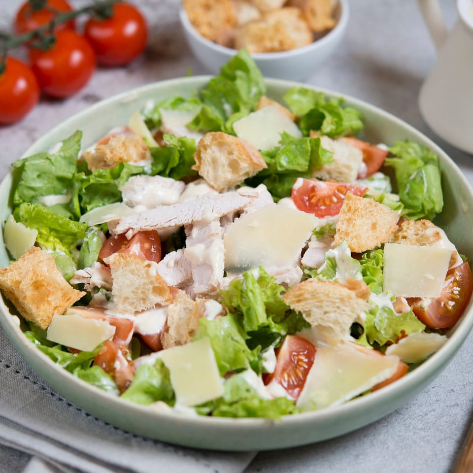 Chicken Caesar salad with lettuce, tomatoes, croutons, parmesan, and dressing in a light green bowl.