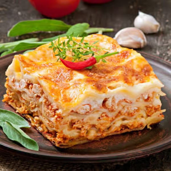 A slice of lasagna with meat sauce, cheese, and herbs on a dark plate.